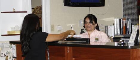 A reception desk with a monitor displaying a video feed, a counter, and a person interacting with the staff member.