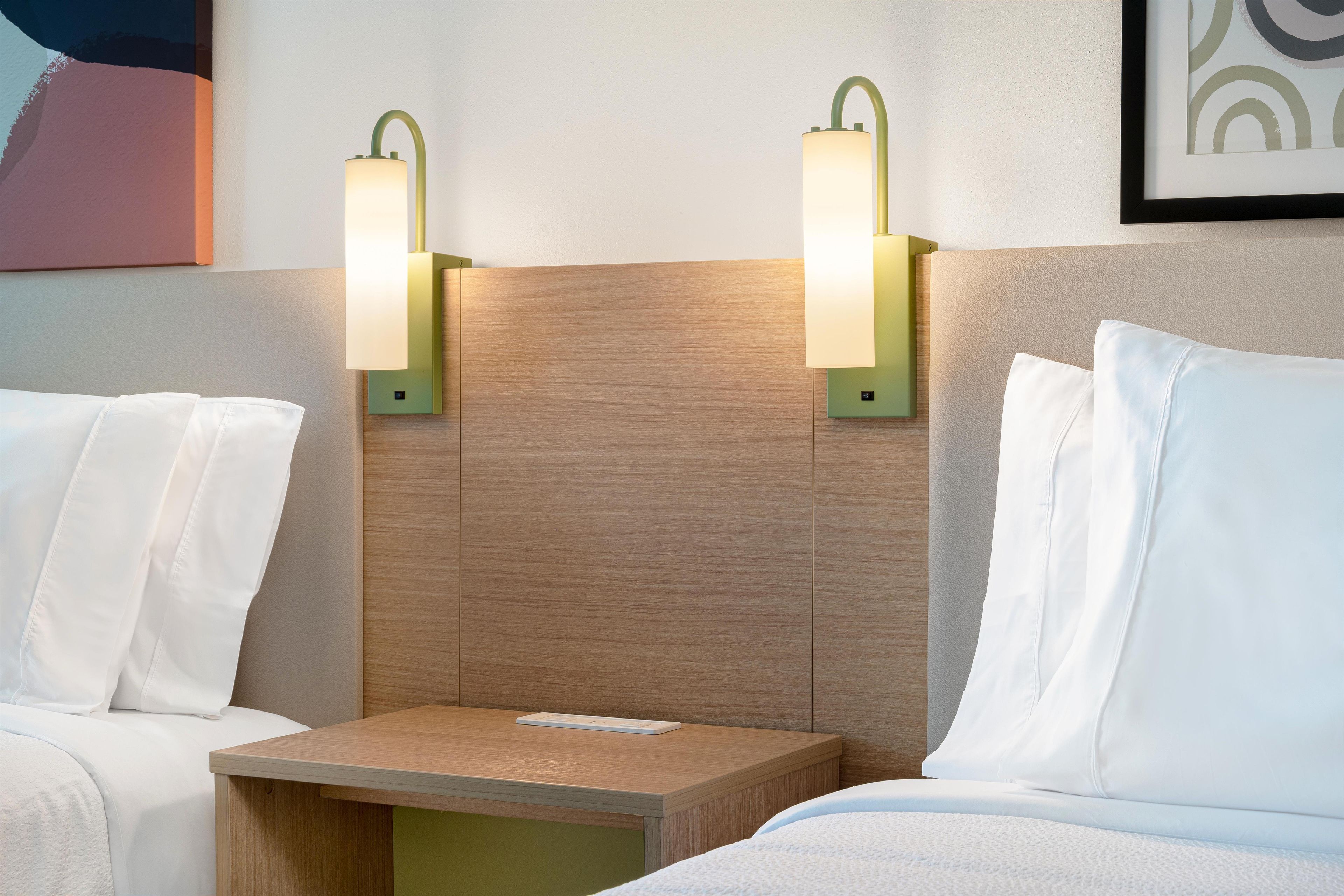 A hotel room with two beds, a nightstand, and wall-mounted reading lights.