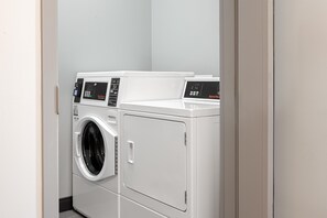 A laundry area with two front-loading washing machines and a dryer. - Spark by Hilton Douglasville Atlanta West (Douglasville)