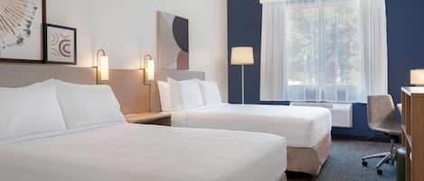 A hotel room with two beds, a desk, a chair, and a window with curtains.
