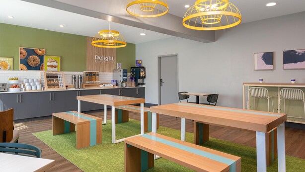 A café with wooden tables and benches, a counter with food items, and a sign that reads 'Delight in the day'. - Spark by Hilton Douglasville Atlanta West (Douglasville)