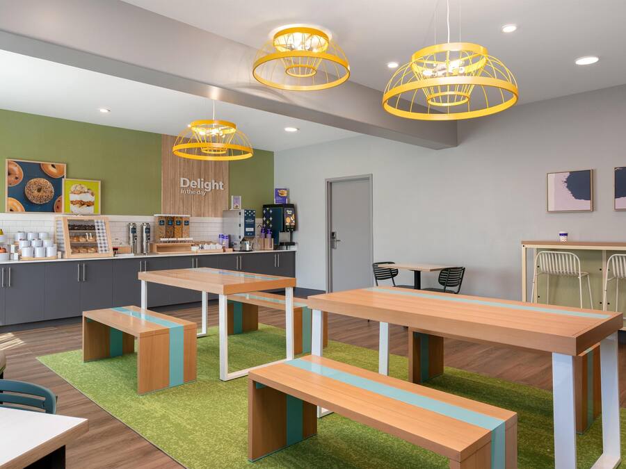A café with wooden tables and benches, a counter with food items, and a sign that reads 'Delight in the day'.