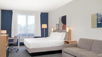 Une chambre d’hôtel avec un lit, un bureau, une chaise, un canapé et une grande fenêtre avec des rideaux.