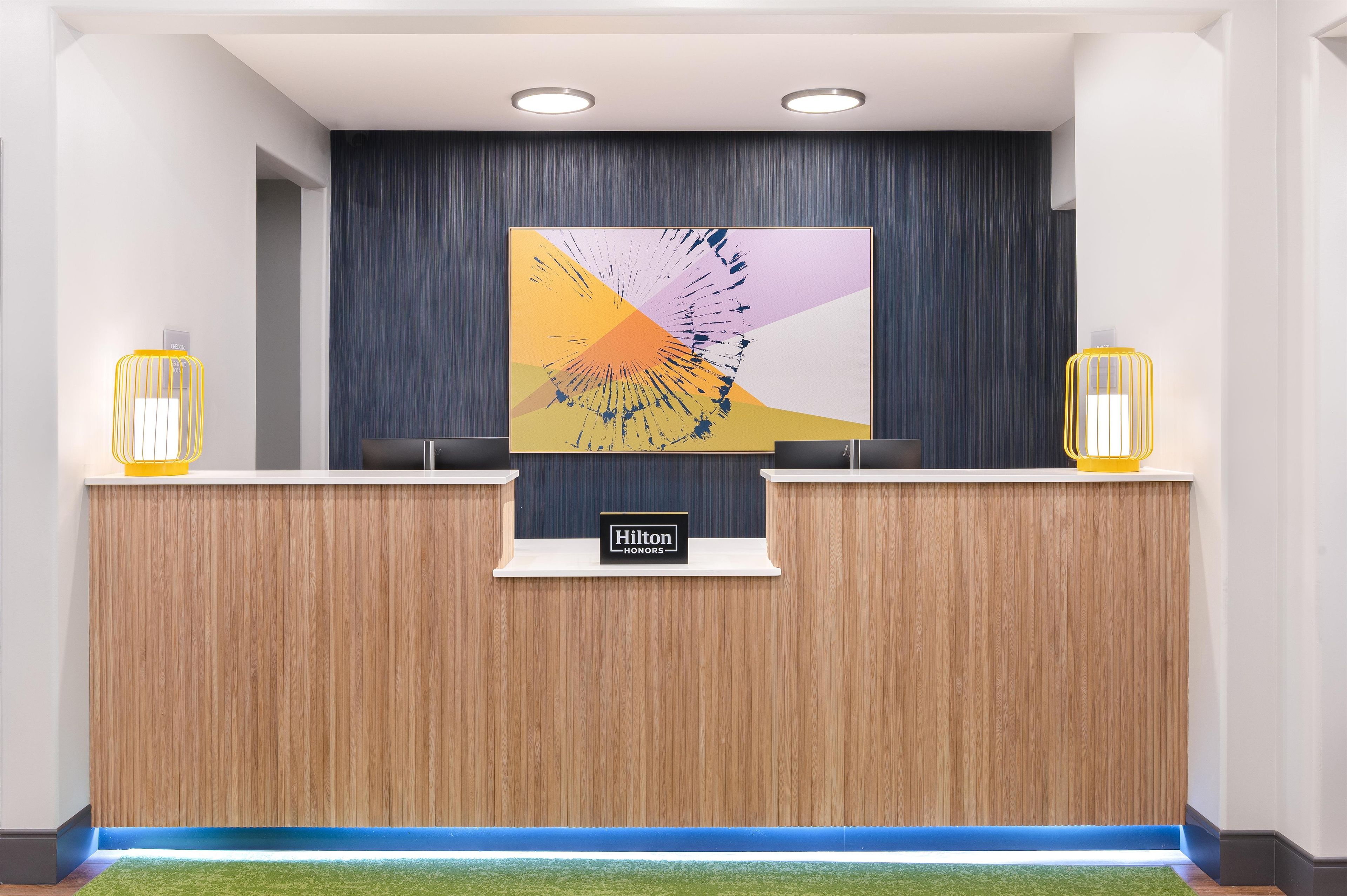 A hotel reception desk with a modern design, featuring a wooden finish and a large abstract painting above it.