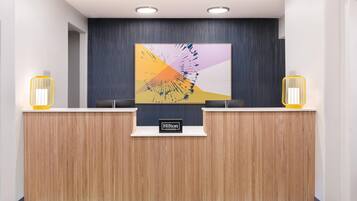 A hotel reception desk with a modern design, featuring a wooden finish and a large abstract painting above it.