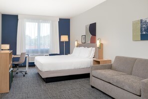 A hotel room with a bed, a desk, a chair, a sofa, and a large window with curtains. - Spark by Hilton Douglasville Atlanta West (Douglasville)