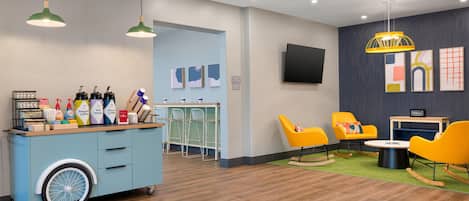 A hotel lobby with a coffee station, seating area, and a TV mounted on the wall.