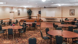 A conference room with multiple tables and chairs, a stage with a podium, and a whiteboard.