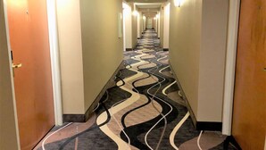 A hotel hallway with a patterned carpet, doors on both sides, and overhead lighting.