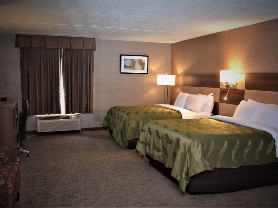 A hotel room with two beds, a desk, a chair, a lamp, and a picture on the wall.