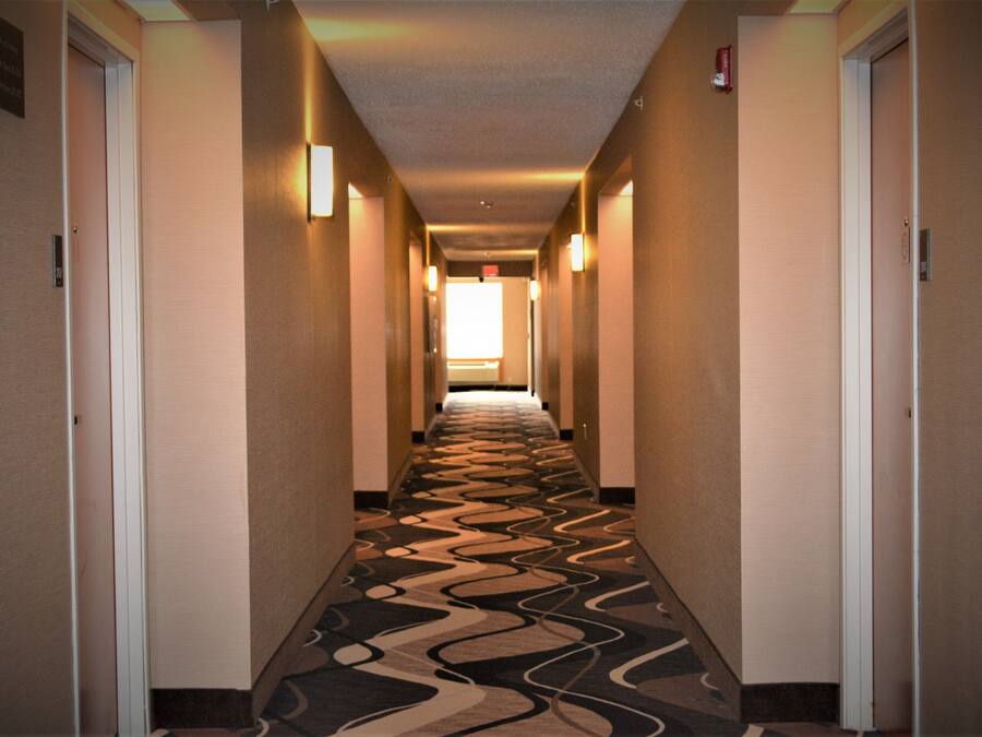 A hotel hallway with patterned carpet, doors on both sides, and wall-mounted lights.