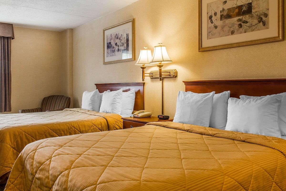 Una habitación de hotel con dos camas, una mesita de noche con lámpara y un cuadro enmarcado en la pared.