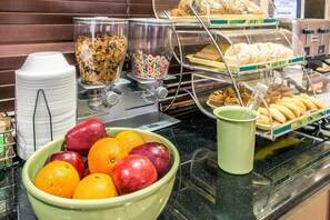 Un área de bufé con diversos alimentos, entre ellos frutas, cereales y pasteles.