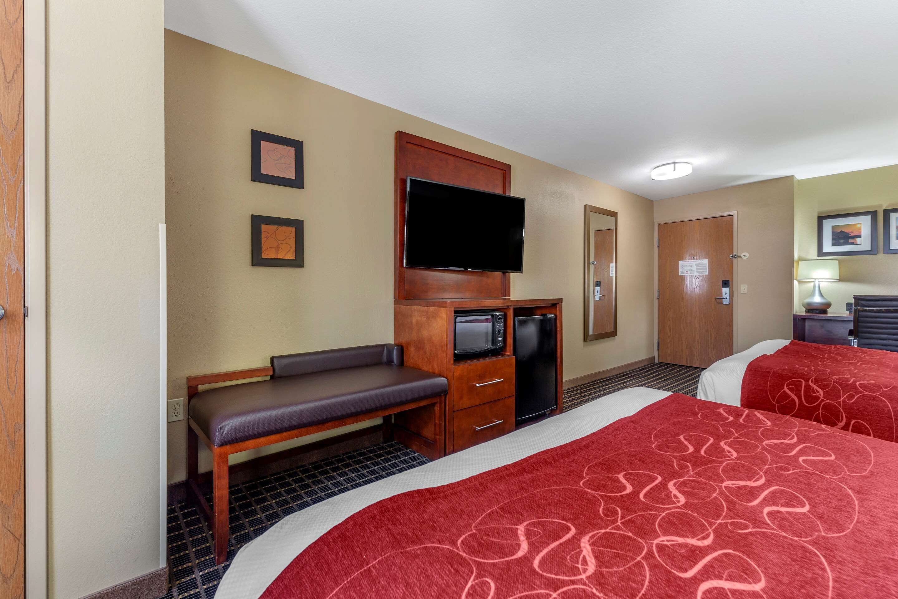 Habitación de hotel con dos camas, televisor, escritorio con microondas y una banca.