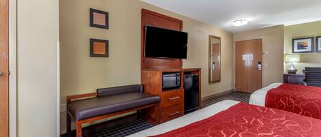 Habitación de hotel con dos camas, televisor, escritorio con microondas y una banca.