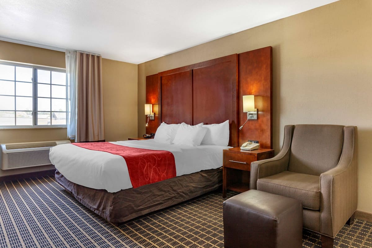 A hotel room with a large bed, a chair, a nightstand, and a window with curtains.