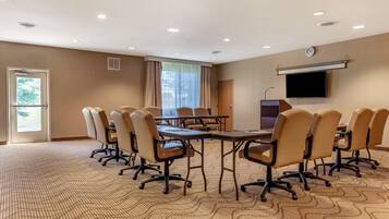 A conference room with a large table, multiple chairs, a television, and a clock on the wall.