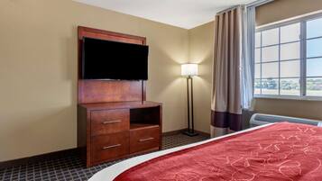 Une chambre d’hôtel avec un lit, un téléviseur fixé à un meuble en bois, une lampe sur pied et une fenêtre avec des rideaux.
