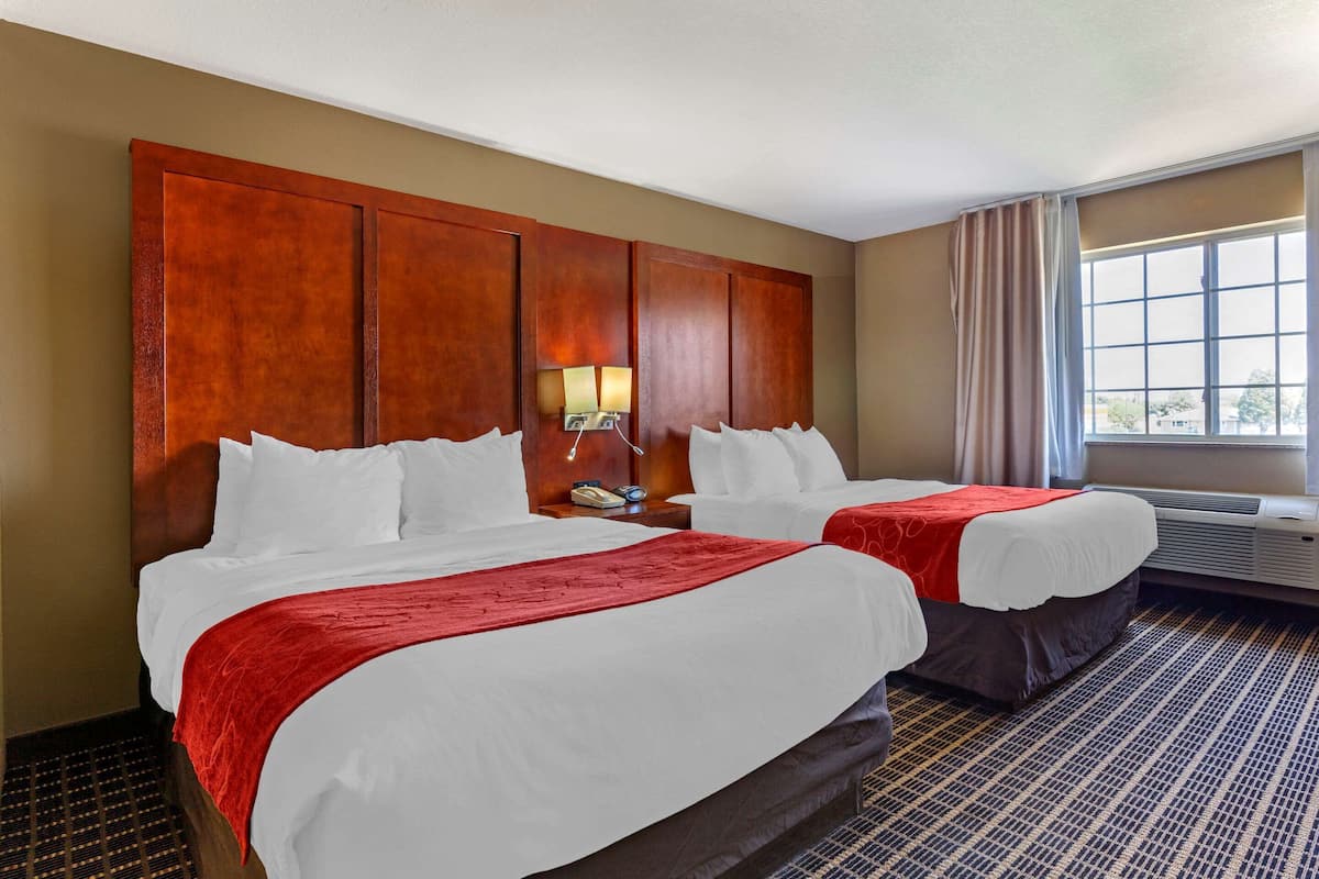 A hotel room with two beds, a wooden headboard, a window with curtains, and an air conditioning unit.