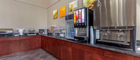 Una cocina moderna con un refrigerador de acero inoxidable, microondas y cafetera. Cuenta con gabinetes de madera y una encimera de granito.