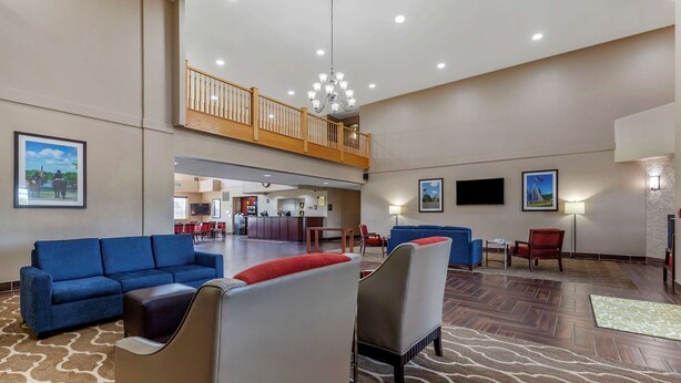 A spacious lobby with a high ceiling, a wooden balcony, and a central seating area with sofas and armchairs. - Comfort Suites Delavan - Lake Geneva Area (Delavan)