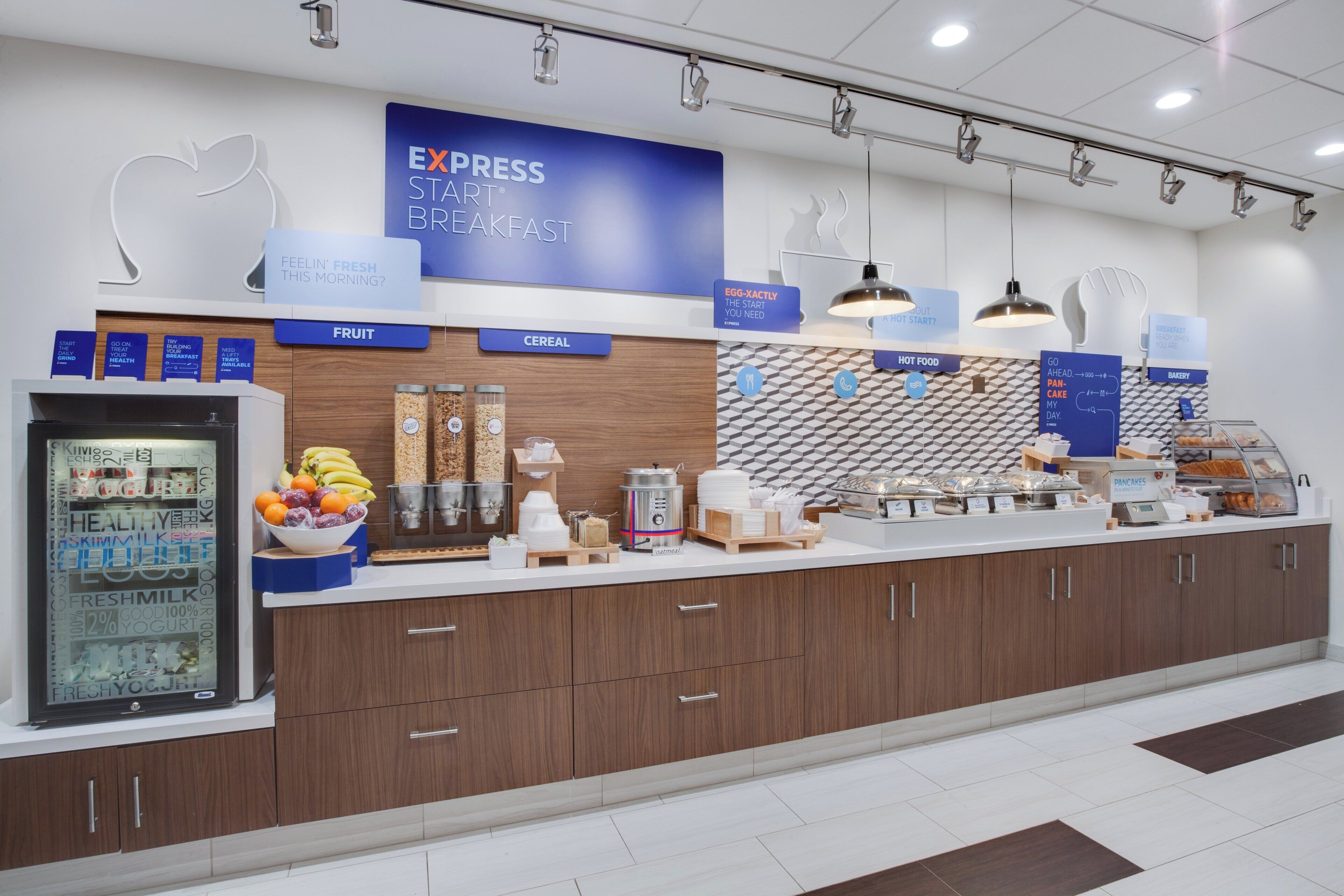 A breakfast area with a sign reading 'EXPRESS START BREAKFAST' and various food options like fruit, cereal, and hot food.