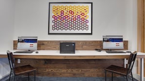 Un espacio de trabajo con dos monitores, una impresora central y una obra de arte abstracta enmarcada en la pared.