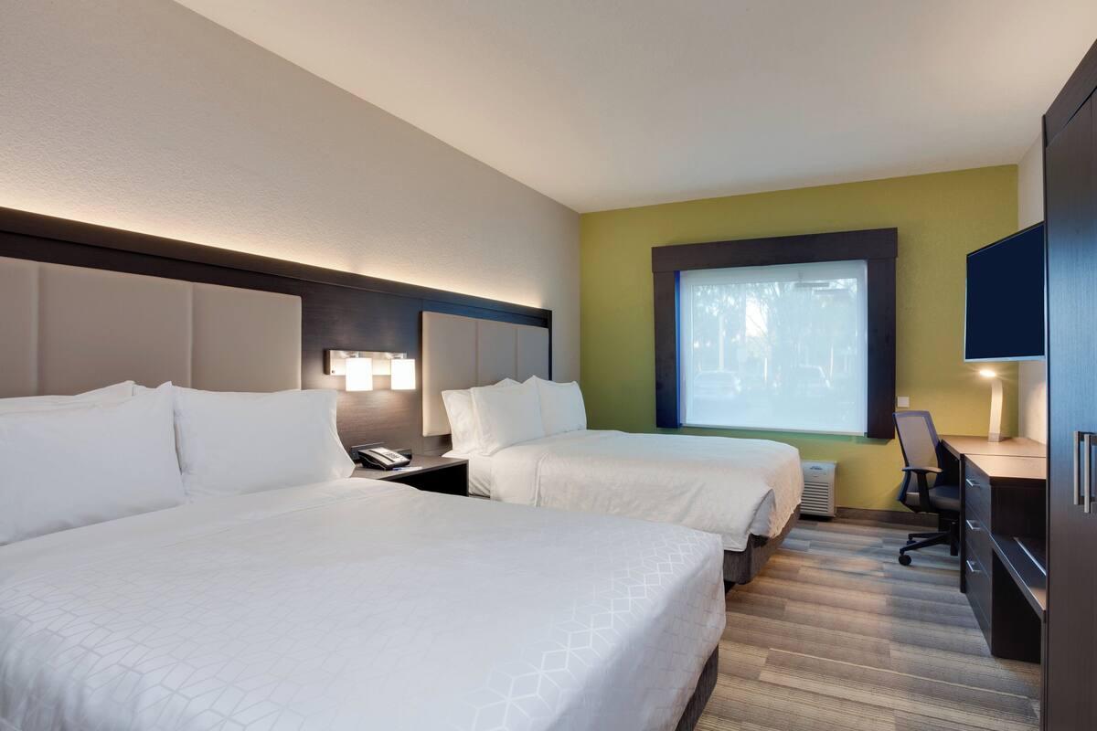Una habitación de hotel con dos camas, un escritorio, una silla, un ventanal grande y un televisor.