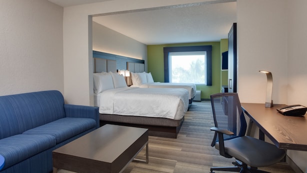 Una habitación de hotel con un sofá azul, un escritorio de madera, una silla, dos camas y un ventanal grande.