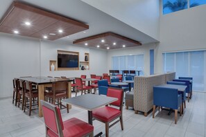 A modern dining area with multiple tables and chairs, a flat-screen TV mounted on the wall, and large windows providing natural light. - Holiday Inn Express Hotel & Suites Ft Lauderdale Airport/Cru by IHG (Fort Lauderdale)