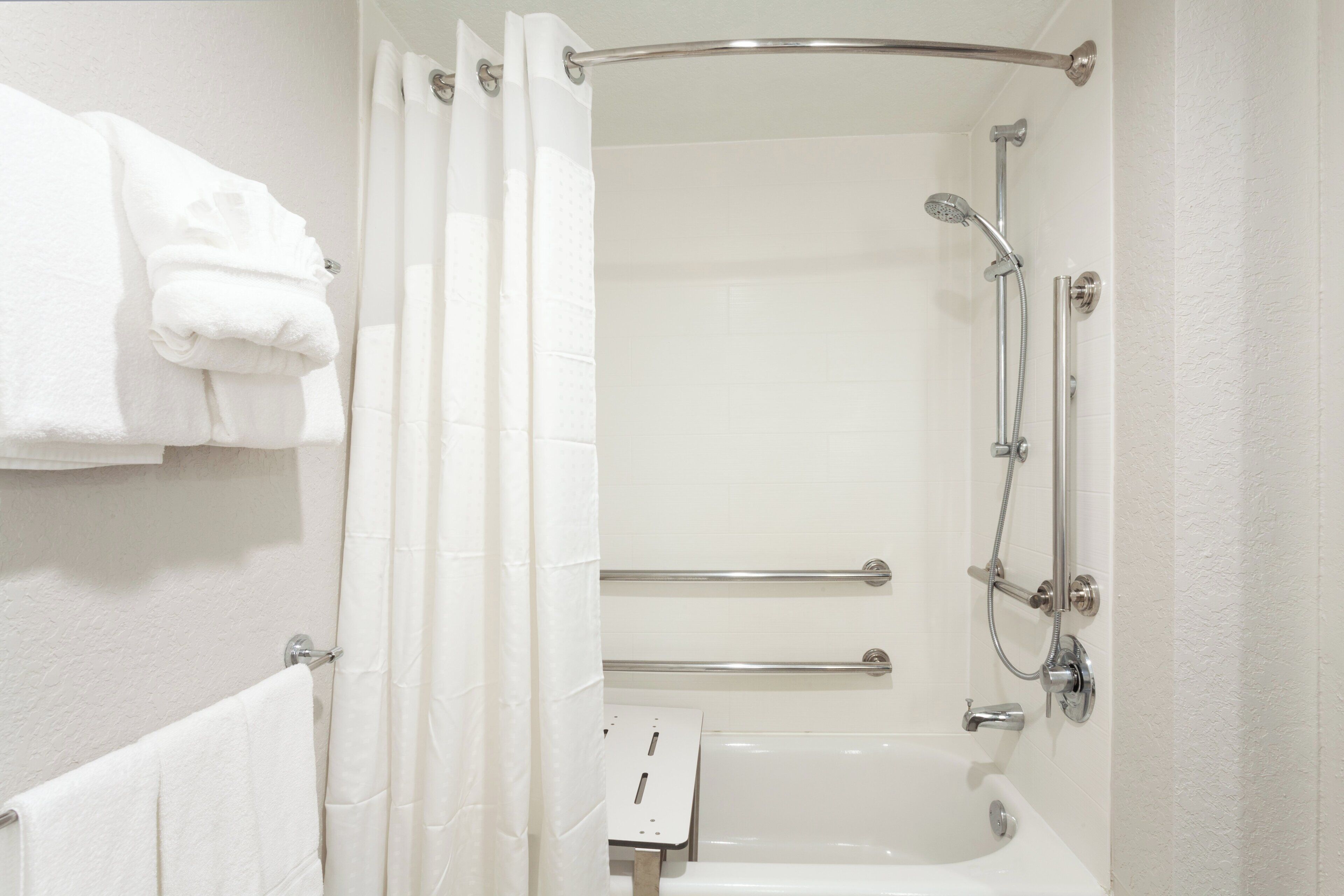 A bathroom with a shower, a bathtub, and a towel rack with folded towels.