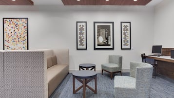 Habitación de hotel con sofá, dos sillones, una mesita redonda y un escritorio con una computadora. Hay tres obras de arte enmarcadas en la pared.