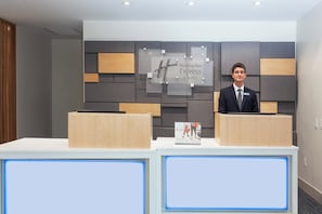 Una recepción de hotel con diseño moderno, un letrero de Holiday Inn Express & Suites y un cartel de bienvenida para IHG.