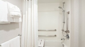 Un baño con bañera, ducha y barras de apoyo.