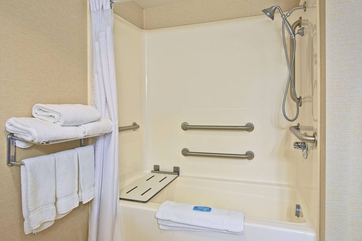 A bathroom with a bathtub, a shower, and two towel racks with folded towels.