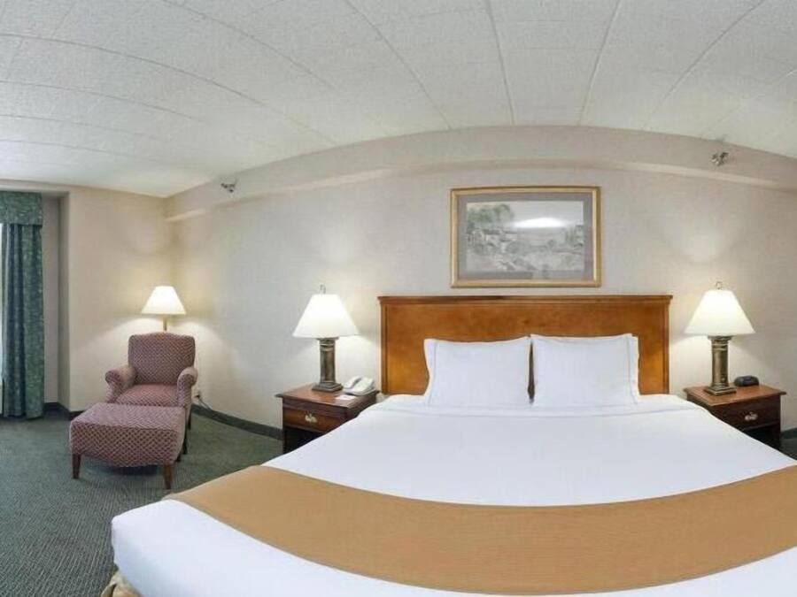A hotel room with a large bed, two bedside tables with lamps, a chair, and a painting on the wall.