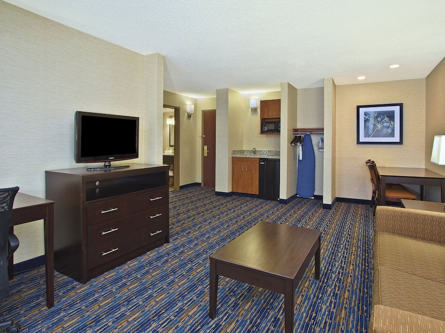 Habitación de hotel con televisión de pantalla plana, escritorio, silla, sofá y kitchenette.