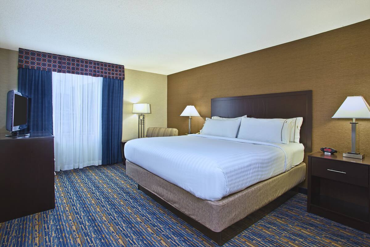 A hotel room with a large bed, two bedside tables with lamps, a TV on a stand, and a patterned carpet.