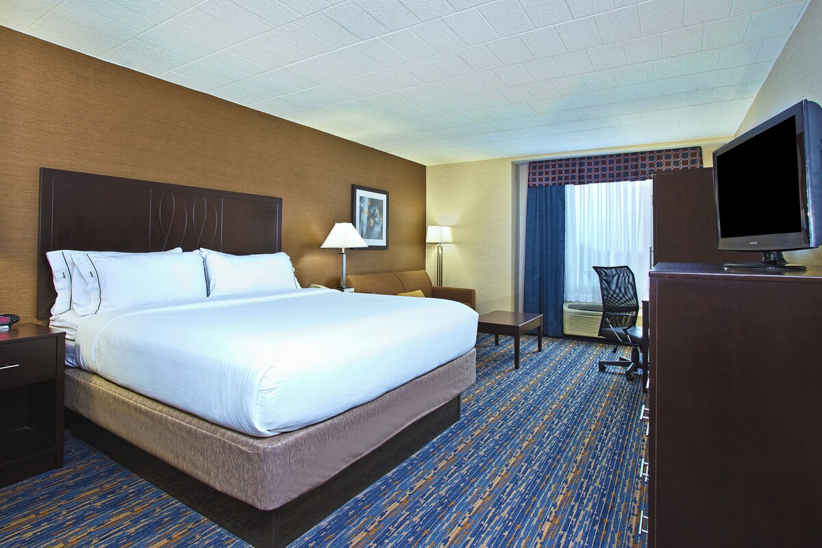 A hotel room with a large bed, a desk, a chair, a television, and a window with curtains.