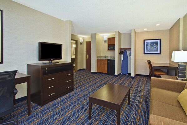 A hotel room with a flat-screen TV, a desk, a sofa, a dresser, and a kitchenette. - Holiday Inn Express Hotel & Suites Pittsburgh West Mifflin by IHG (West Mifflin)
