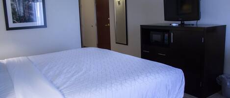 A hotel room with a large bed, a television on a cabinet, a framed picture on the wall, and a door with a light above it.