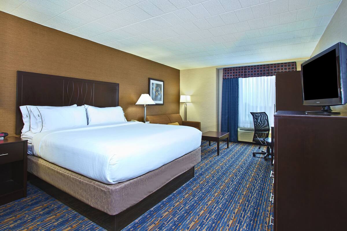 A hotel room with a large bed, a desk, a chair, a television, and a window with curtains.