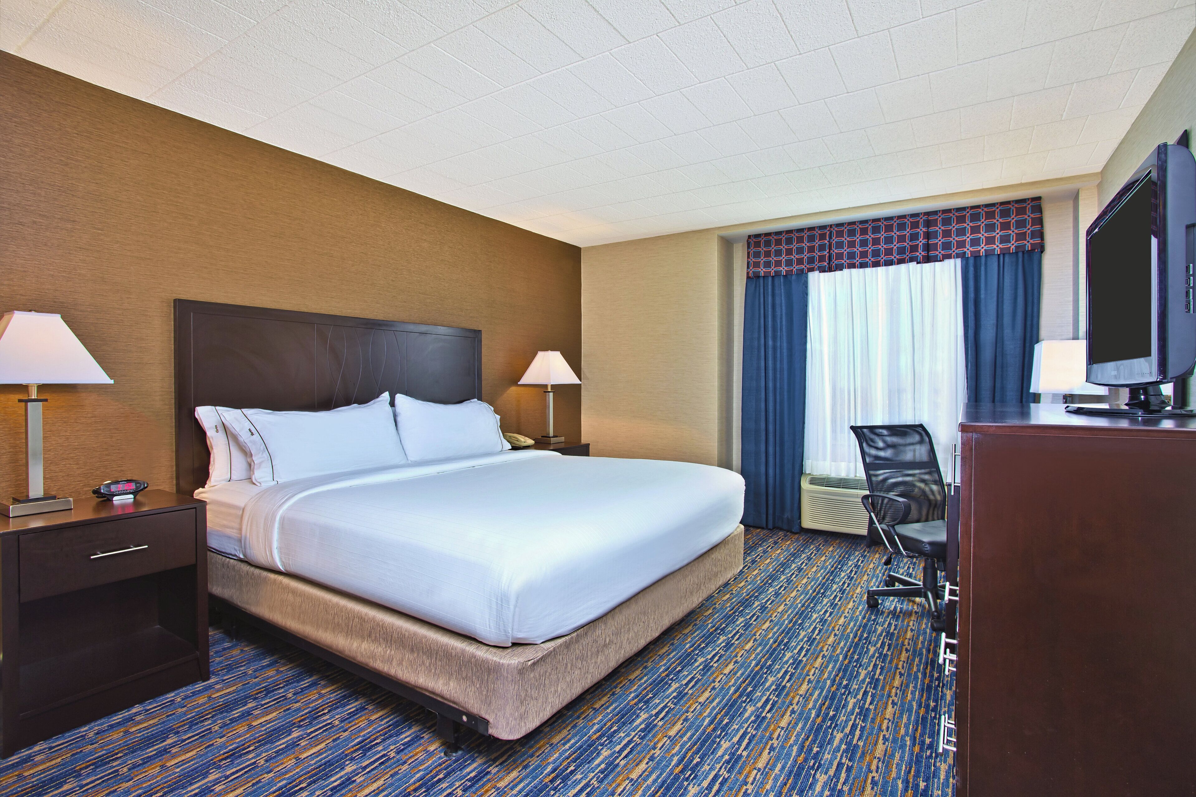 A hotel room with a large bed, two bedside tables with lamps, a desk with a chair, and a television.