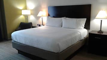 A hotel room with a large bed, two bedside tables with lamps, a chair, and a nightstand with a phone.
