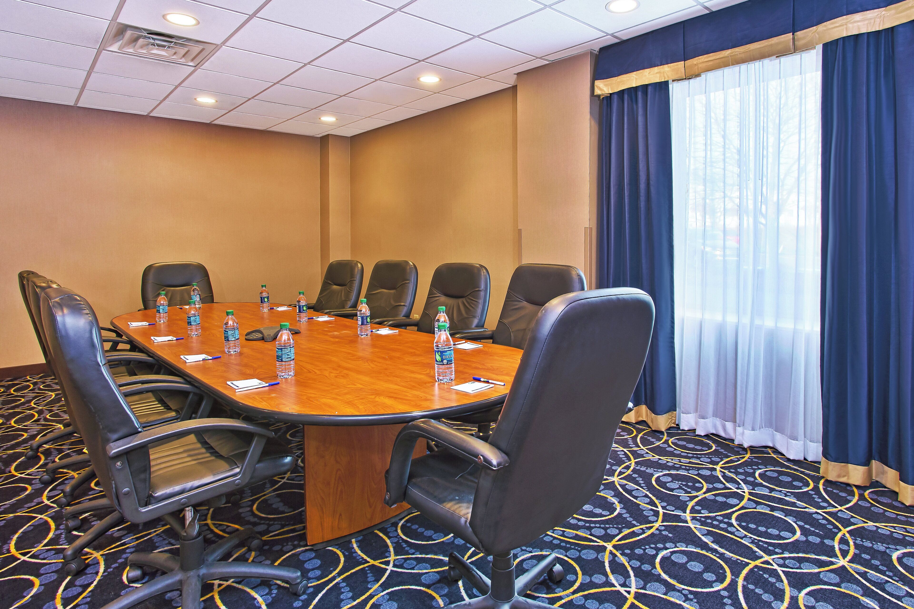 A conference room with a wooden table, black chairs, water bottles, and a patterned carpet.