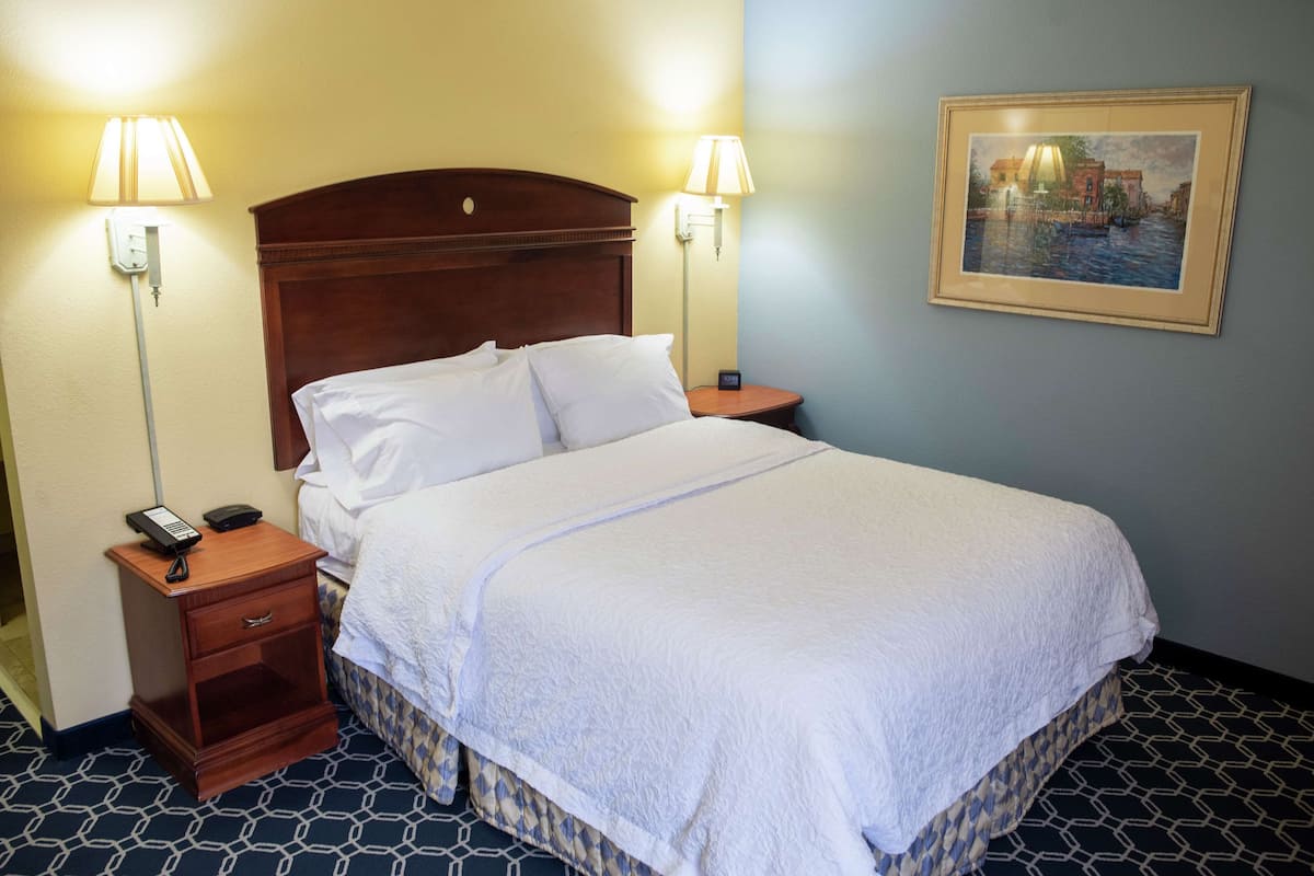 Une chambre d’hôtel avec un grand lit, deux lampes de chevet, une table de chevet avec un téléphone et un tableau au mur.