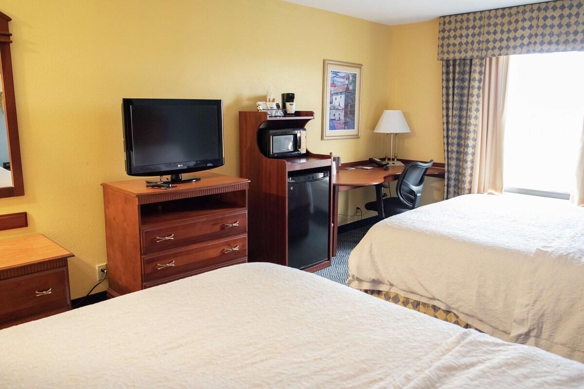 A hotel room with two beds, a desk with a computer, a television, a microwave, and a lamp.