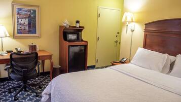A hotel room with a bed, desk, chair, microwave, and a door.