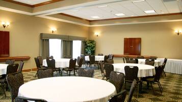 A conference room with round tables and chairs, large windows, and a carpeted floor.