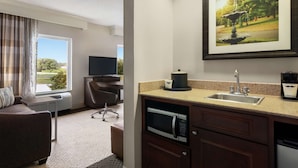 A hotel room with a sofa, a desk with a computer, a microwave, a sink, and a framed picture of a fountain. - Hampton Inn & Suites Montgomery-EastChase (Montgomery)